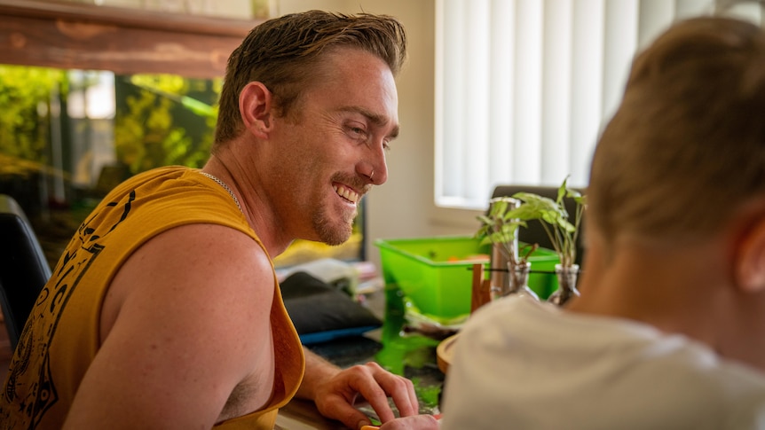 A man with short light brown hair smiles at a child, who is unidentifiable.