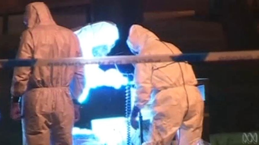 People in hazmat suits look at the ground using blue lights.
