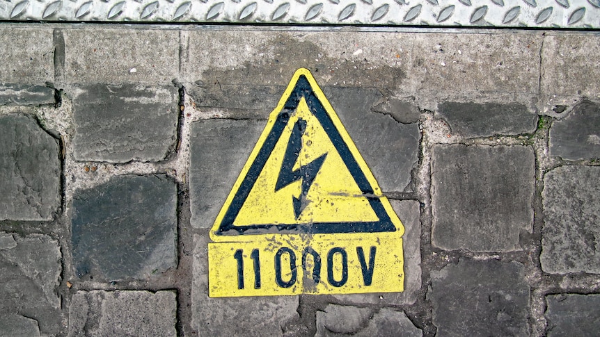 Yellow electric shock warning on a grey brick wall. The sign reads 11000V. The colours of the image are washed out. 