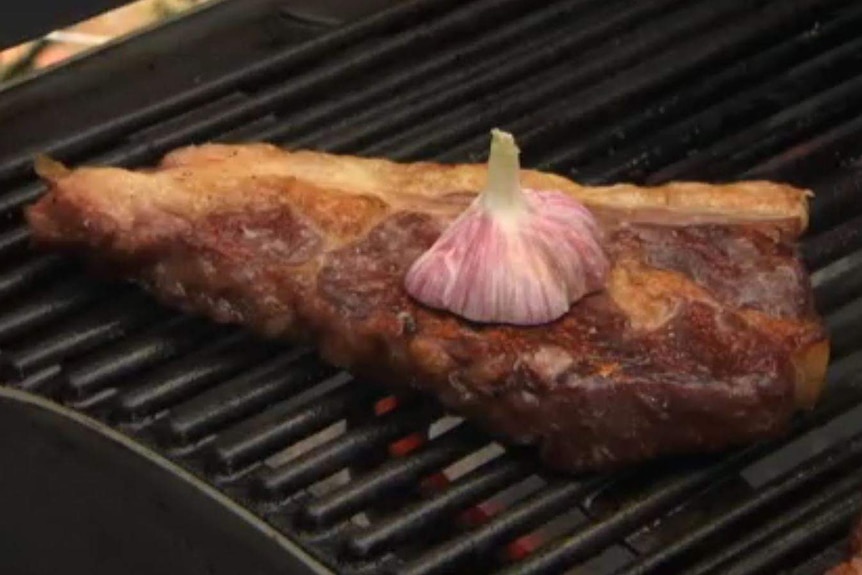 Steak sits on barbecue with garlic.