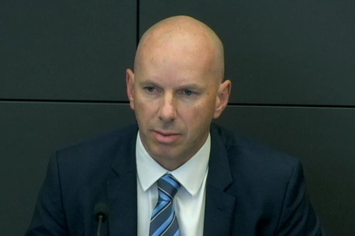 Dressed in suit and tie, Craig Holland sits before a microphone at a hearing of the royal commission.
