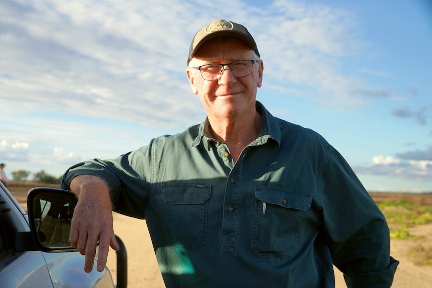 Photo of a man smiling as he leans against the side rear-view mirror of his vehicle 