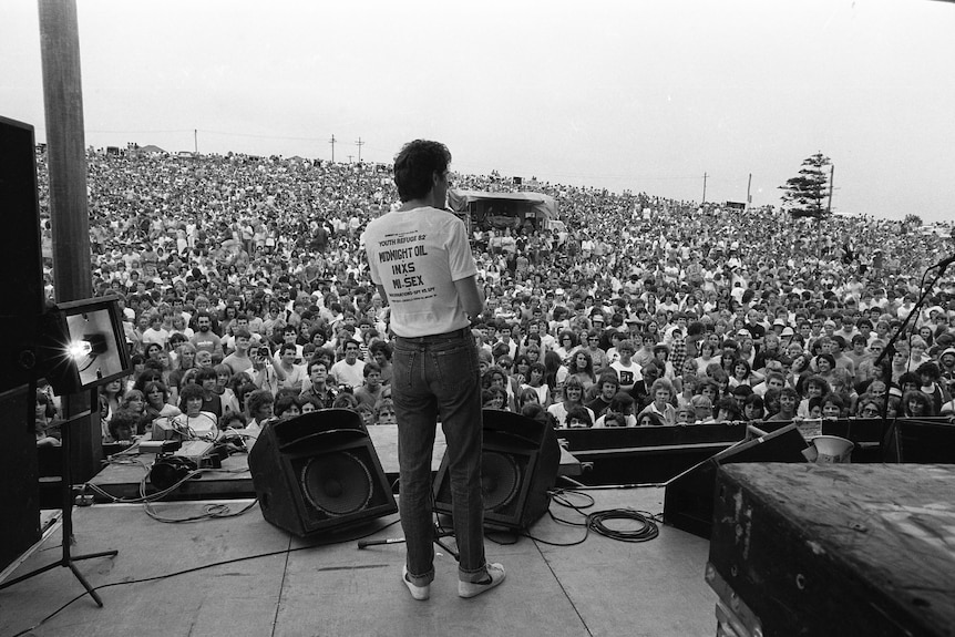 Black and white image of a man on a stage looking out at a huge crowd