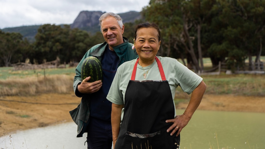 Couple standing on organic farm in front of mountain 