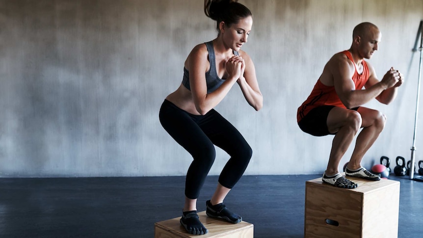 A man and a woman wearing fitness gear jump onto boxes