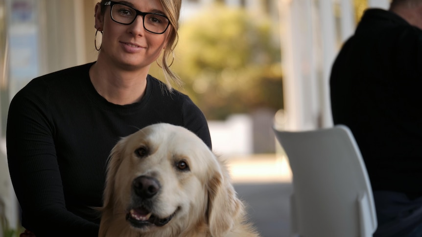 A young woman poses outside a cafe with a large golden retriever dog.