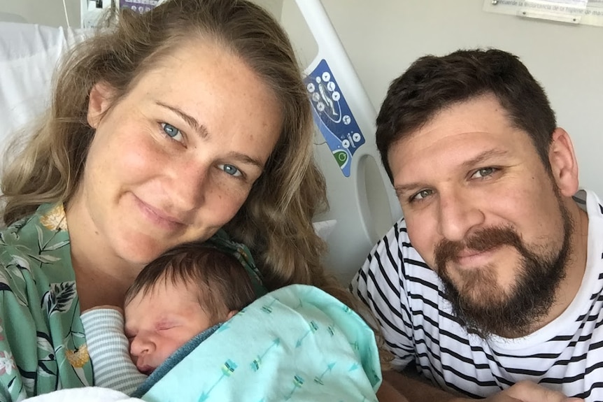 A woman in a hospital bed holding a newborn baby with a man next to her.