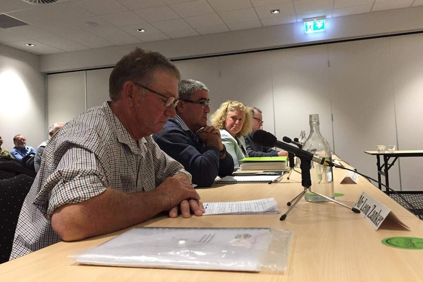 Four graziers sit next to each other at a table to give evidence, some look at notes, others look at each other