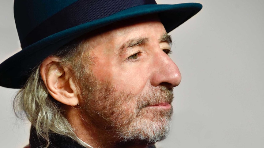 A man with a greying beard, wearing a blue fedora.
