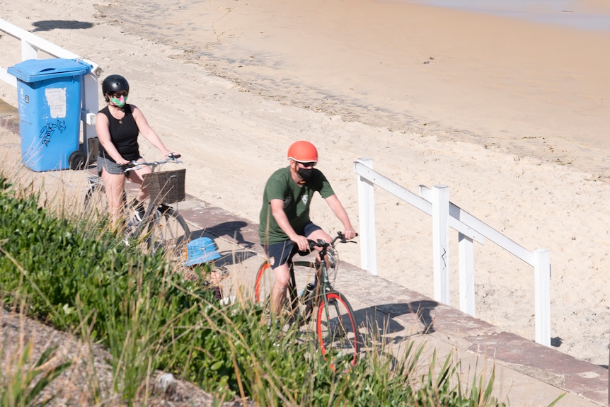 A man and a woman riding their bikes along a beach promenade.