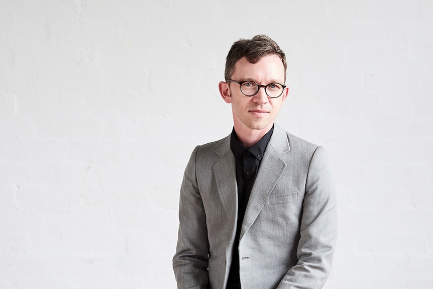 Close-up colour photo of author Robert Lukins in front of plain grey wall.