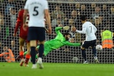 A Premier League striker watches the ball go wide of a diving goalkeeper into the net as fans stare back.