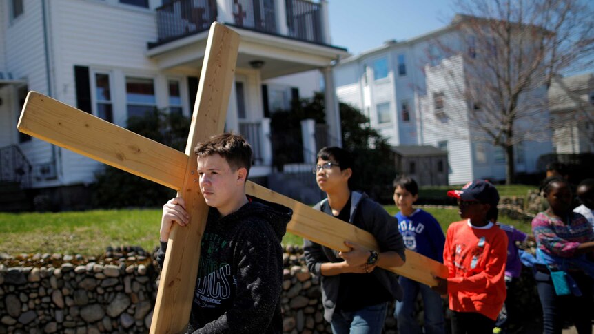 Children in Massachusetts carry a cross between the Catholic Churches in their neighbourhood.
