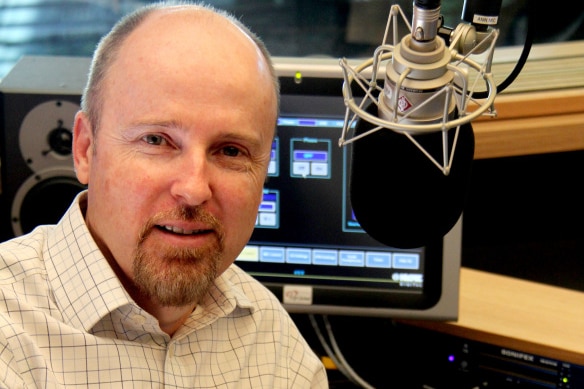 A man sits near a radio studio microphone.