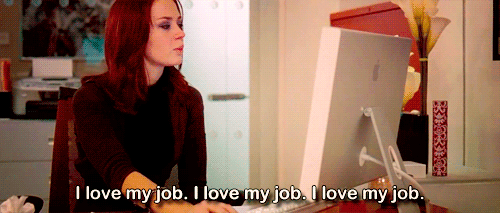 Gif of Emily Blunt in film Devil Wears Prada sitting at office desk, saying 'I love my job' and looking stressed.