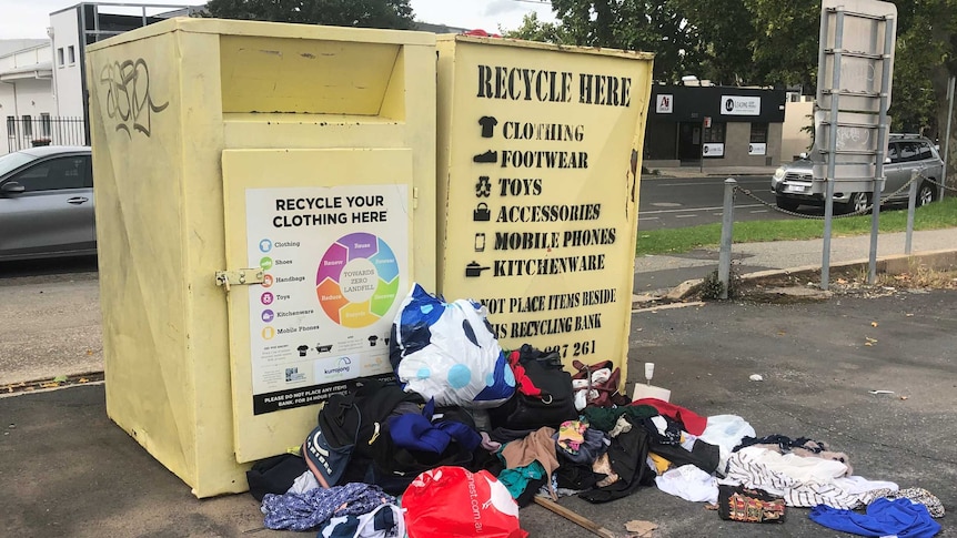 clothes and other donated items on the street next to donation bin