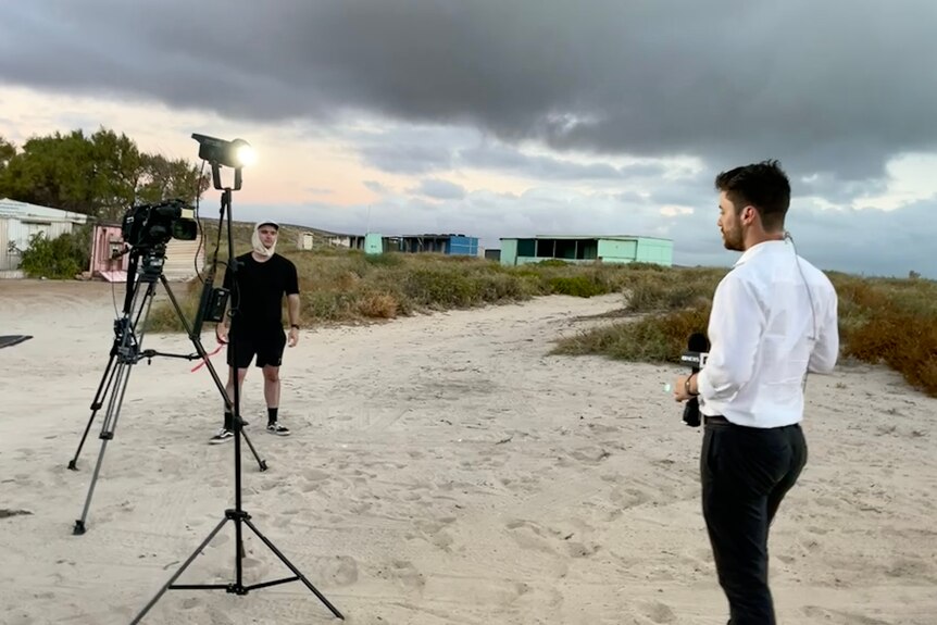 A TV reporter and camera operator stand in a beach side campsite giving a live cross late on a stormy looking day.