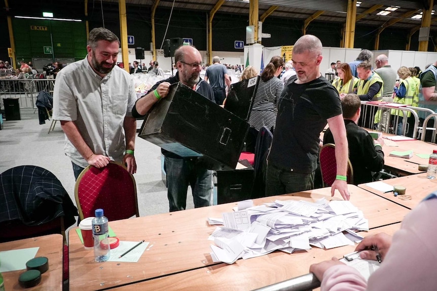 Workers pour ballot papers out onto the table, ready to be counted.