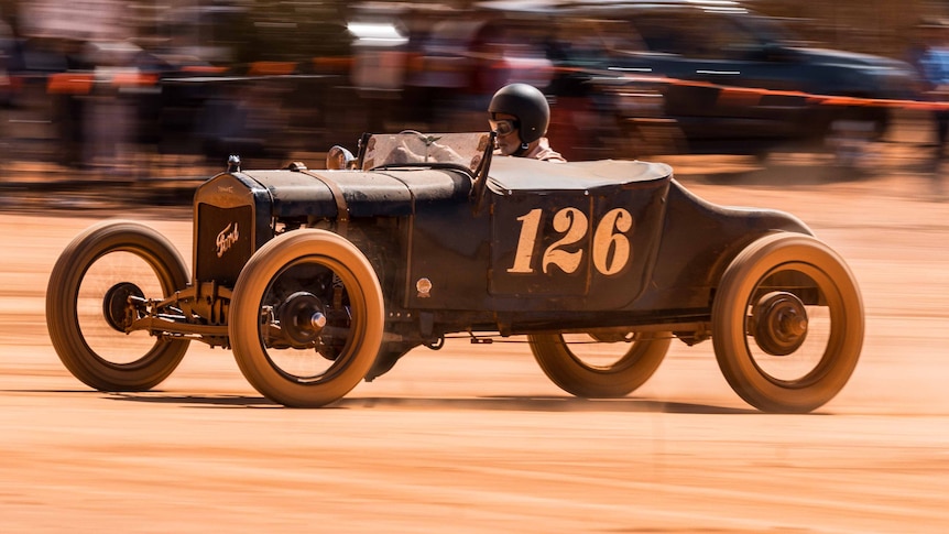 a vintage car racing on a dry, red dirt lake bed. 
