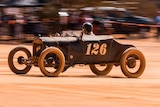 a vintage car racing on a dry, red dirt lake bed. 