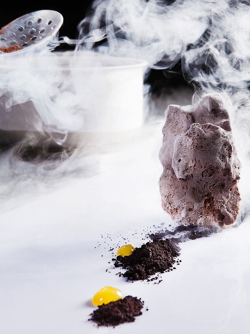 Dry ice floats from saucepan with ladel with rock of chololate ice cream in foreground with edible "soil"