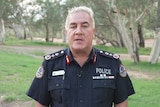 Northern Territory Police Commissioner stands in navy police uniform in front of open green field with gum trees.