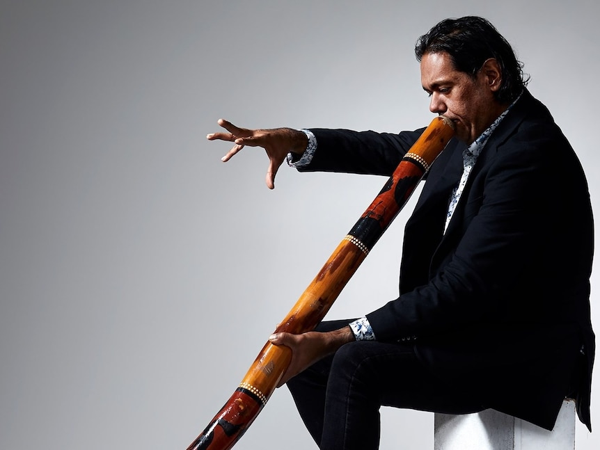 Man plays didgeridoo before a white backdrop