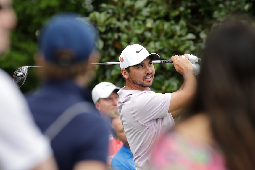 Jason Day hits a shot and smiles as seen between spectators in the foreground