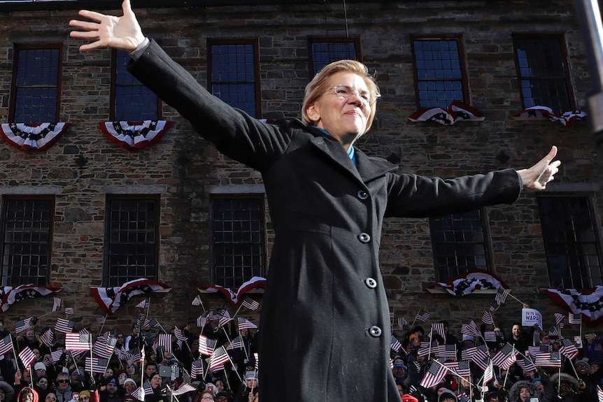 Senator Elizabeth Warren wears a black coat with arms outstretched to acknowledge supporters at the launch of her campaign