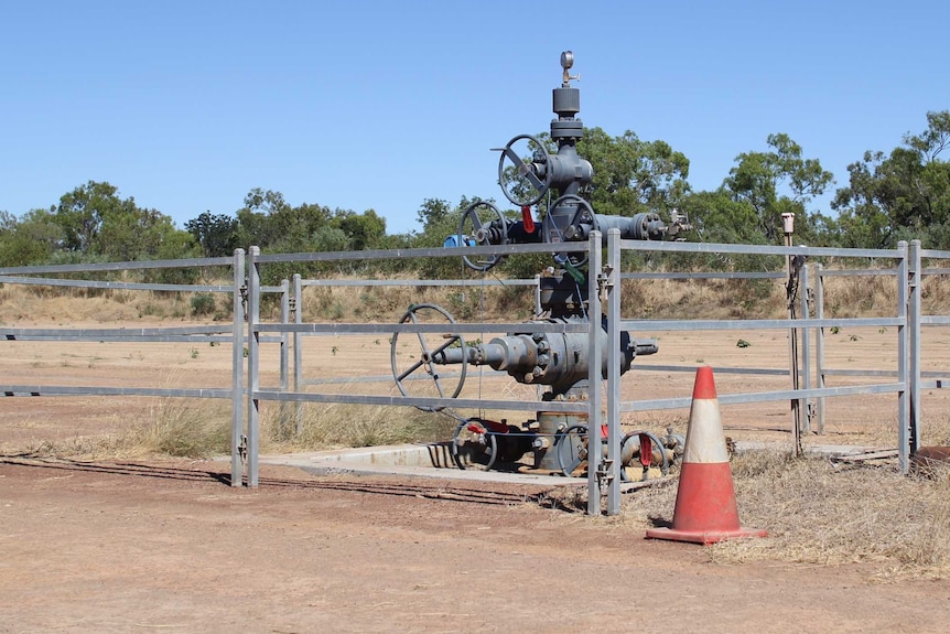 a well head surrounded by a fence in a cleared patch of scrub