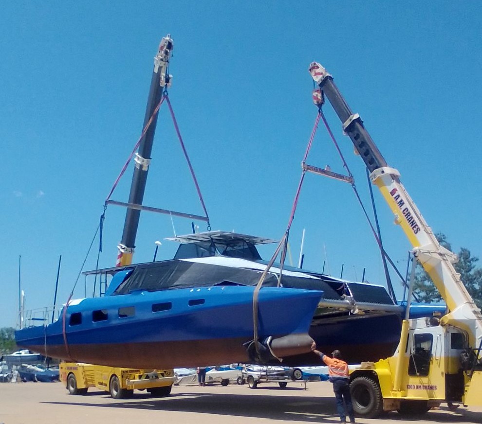 large blue catamaran sits on top of yellow crane