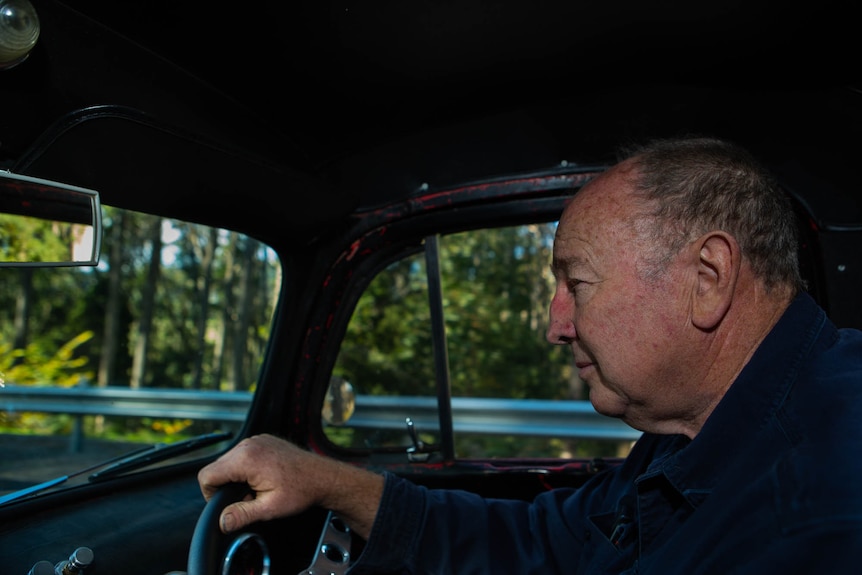 A man at the wheel driving along a Tasmanian back road, trees and ferns visible through windows.