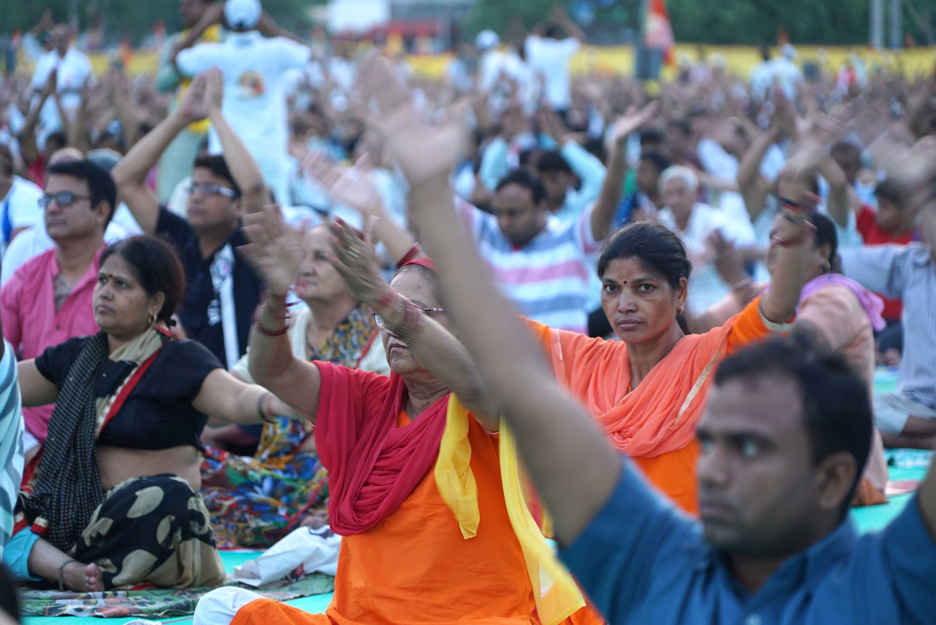 A crowd of people sitting cross-legged raise their hands in the air.
