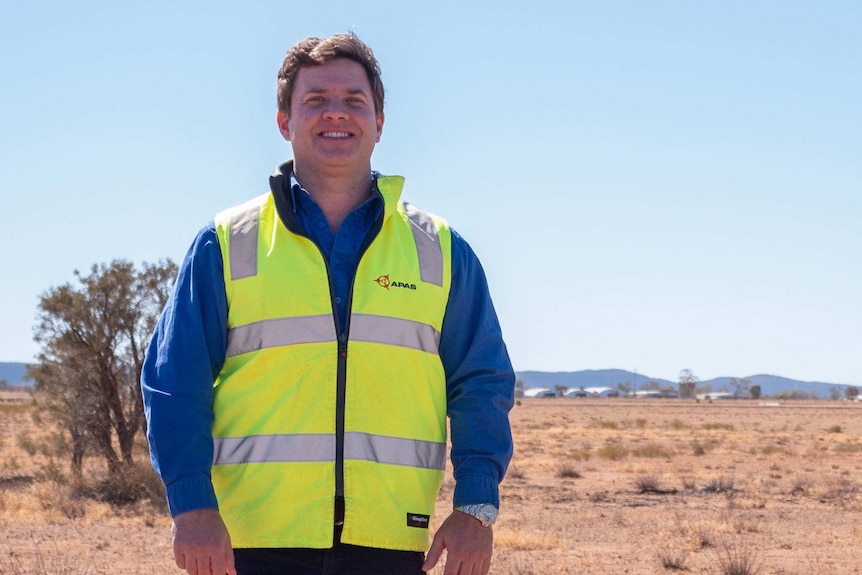 Tom Vincent is wearing a bright vest and looking happy. He is outdoors in Central Australia.