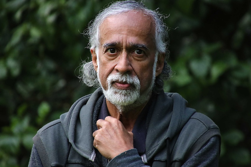 A headshot of Suresh Rajan wearing a grey jumper in front of some trees.