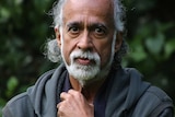 A headshot of Suresh Rajan wearing a grey jumper in front of some trees.