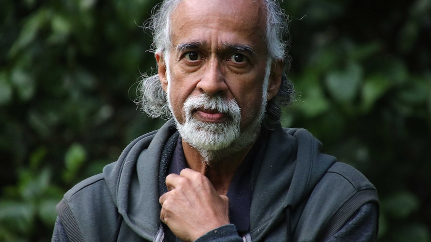 A headshot of Suresh Rajan wearing a grey jumper in front of some trees.