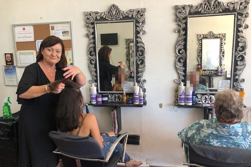 Sonia Colvin brushes a client's hair in front of two silver mirrors on the wall.