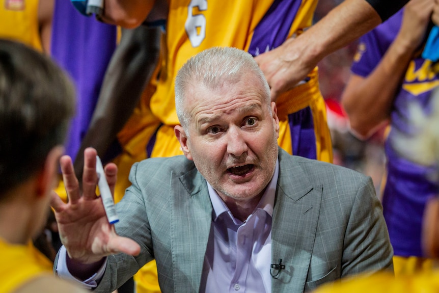 A basketball coach gestures with his hand as he gives a team talk to players around him during an NBL game.