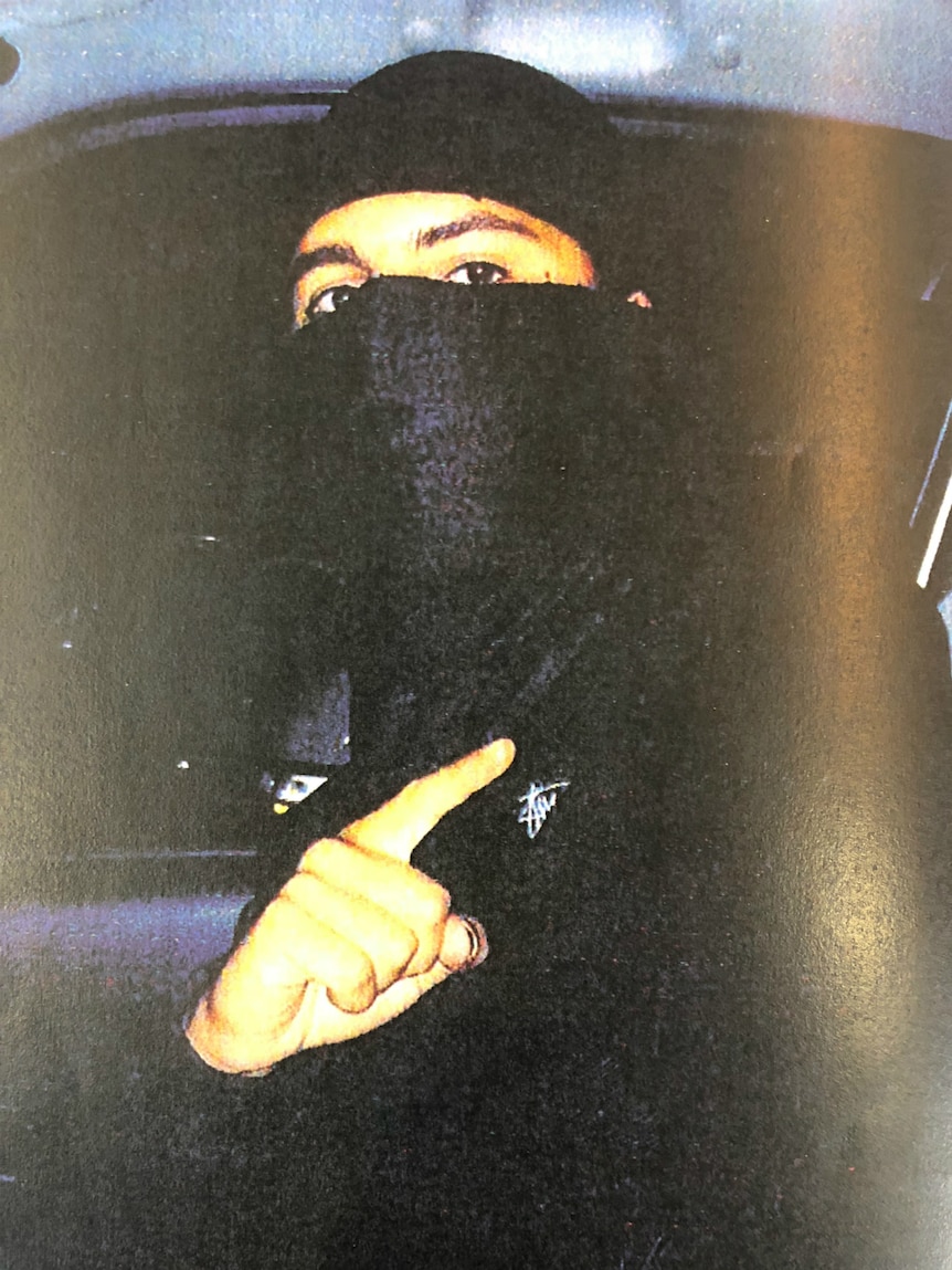 A man with all parts of his face covered with a black garment except his eyes, looks at the camera