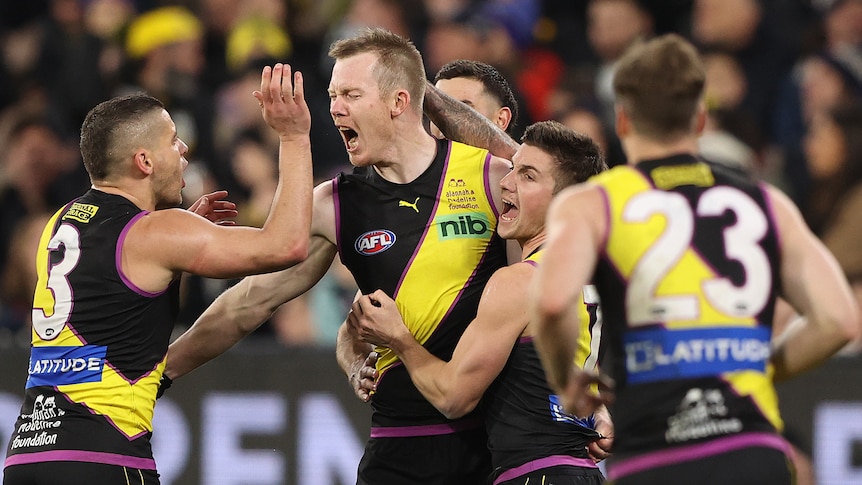 A Richmond forward roars in triumph as his teammates surround him after a goal at the MCG.