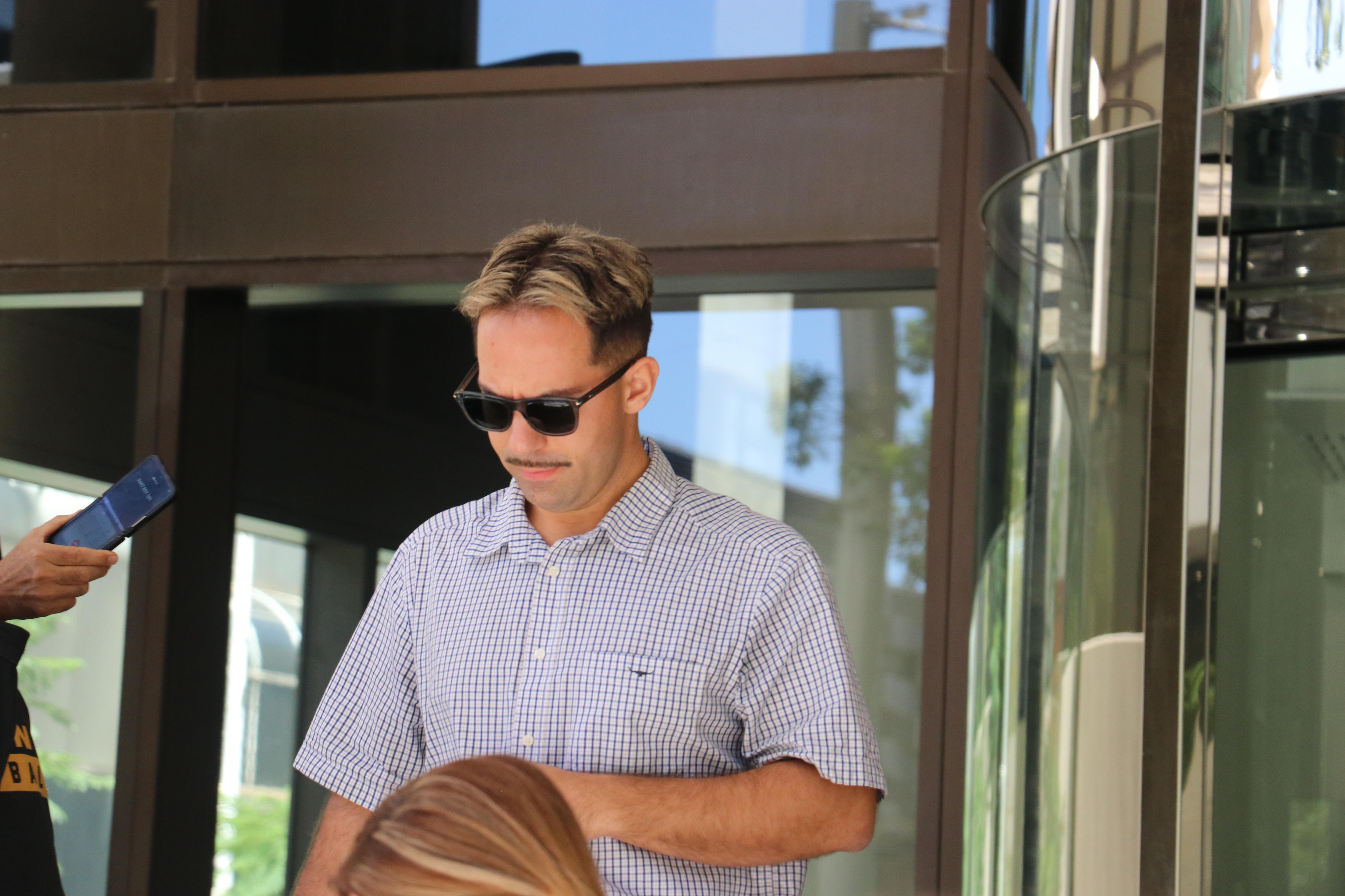 A man wearing sunglasses and short sleeved dress shirt looking down