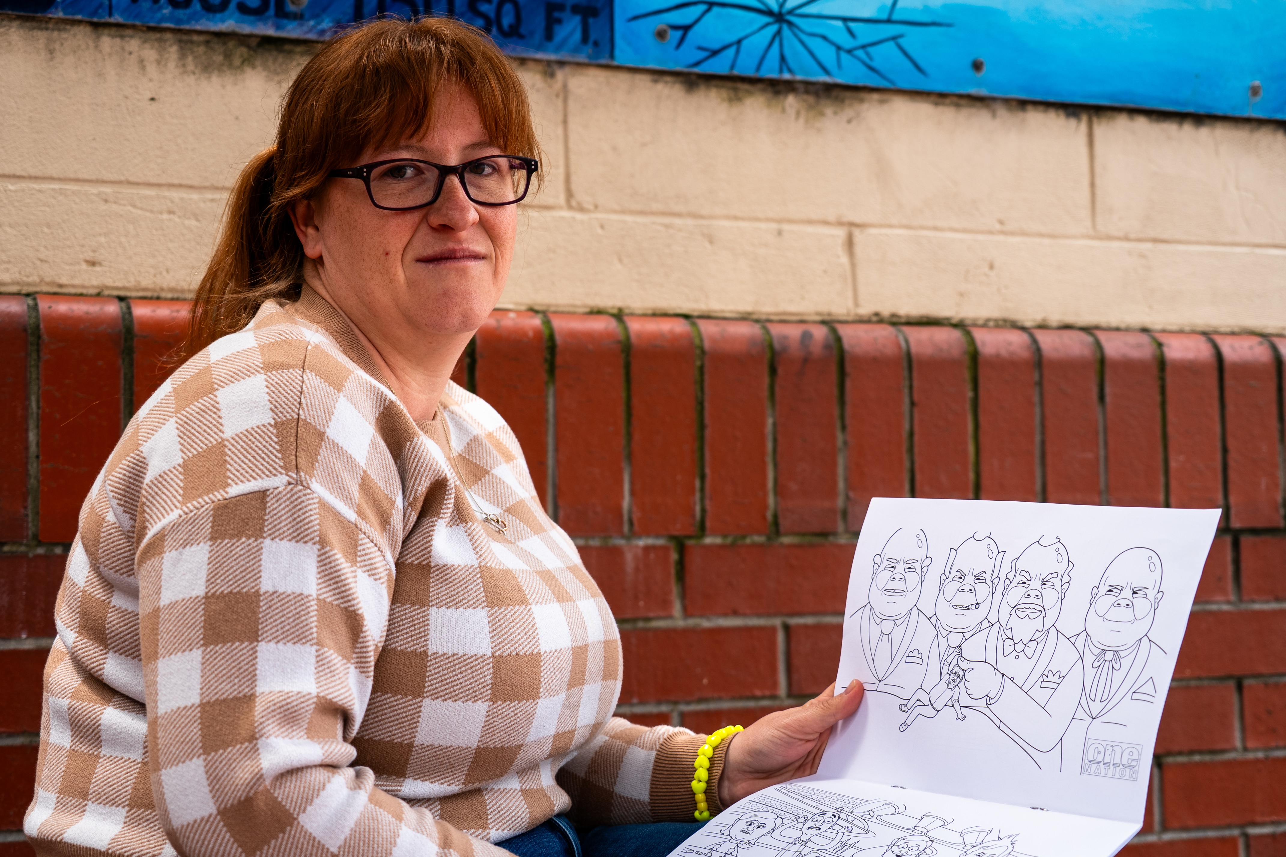 a woman looks displeased holding a colouring book with political imagery inside