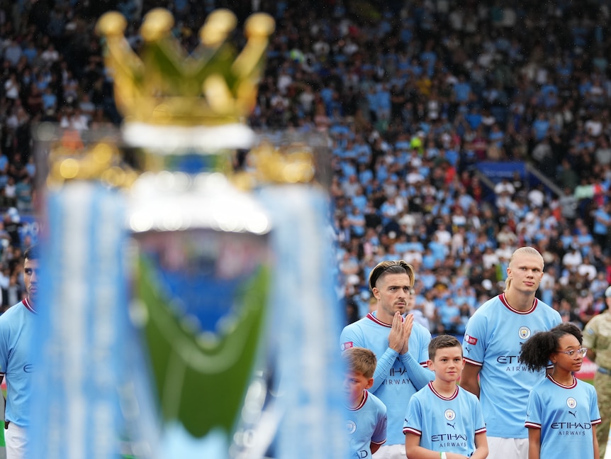 Male soccer players wearing light blue stand behind a trophy