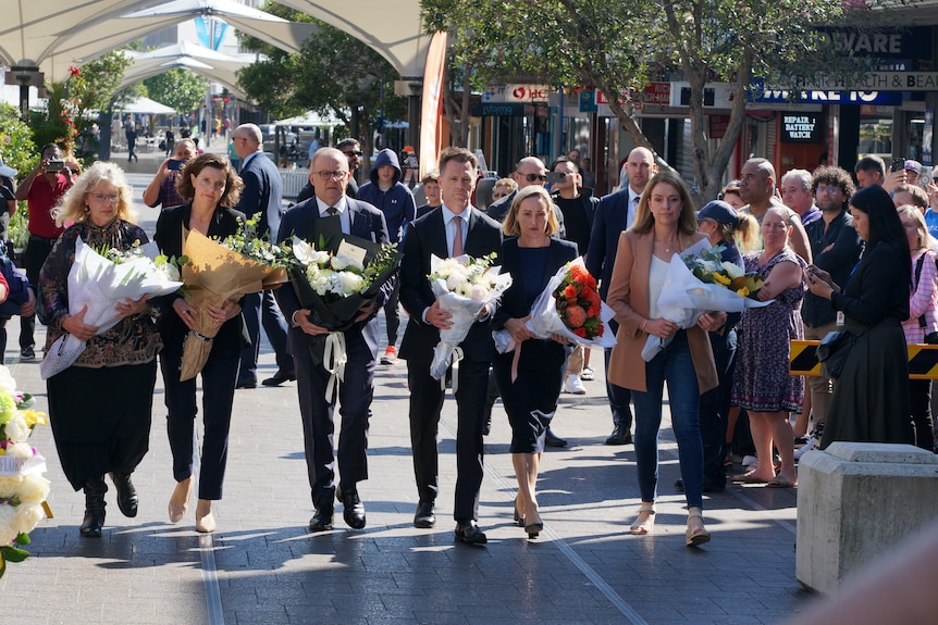 Anthony Albanese and Chris Minns carrying flowers surrounded by crowds
