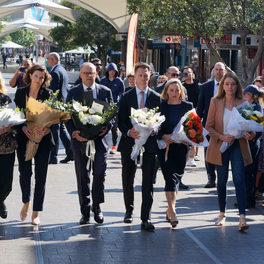Anthony Albanese and Chris Minns carrying flowers surrounded by crowds