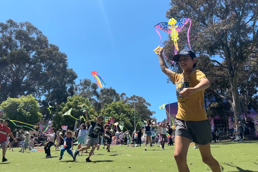 A child runs holding a kite in the foreground as many others do the same in the background.