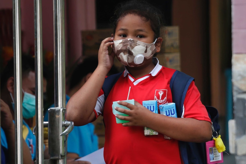 A young girl puts on her protective face mask as she leaves school during high levels of air pollution in Bangkok.