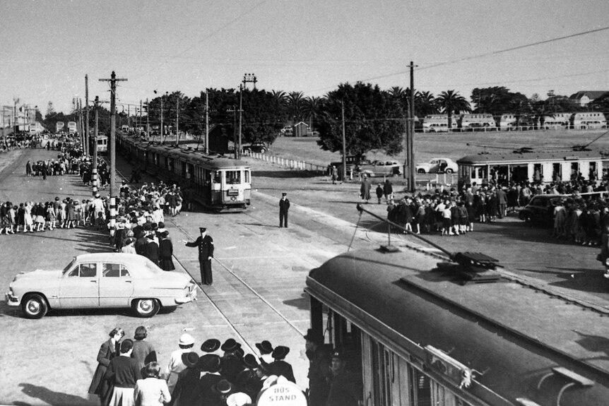 Archive photo of trams running along a street surrounded by crowds pf pedestrians waiting to get on them