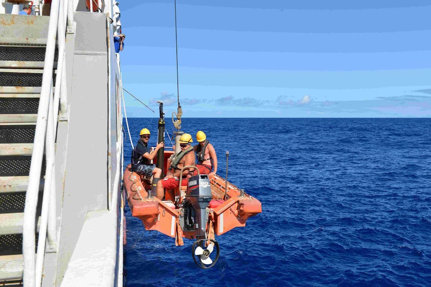 Three researchers in a small boat on the side of a ship lower a bio-Argo - or floating sea robot - into the Indian Ocean.
